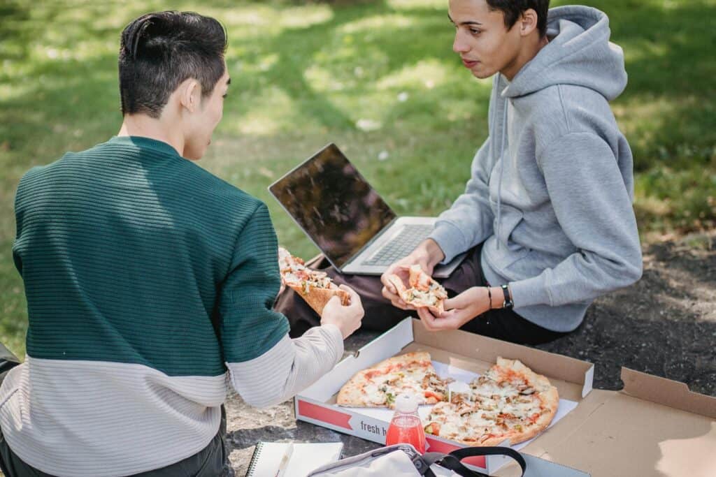 Male college students studying together in a park while eating pizza