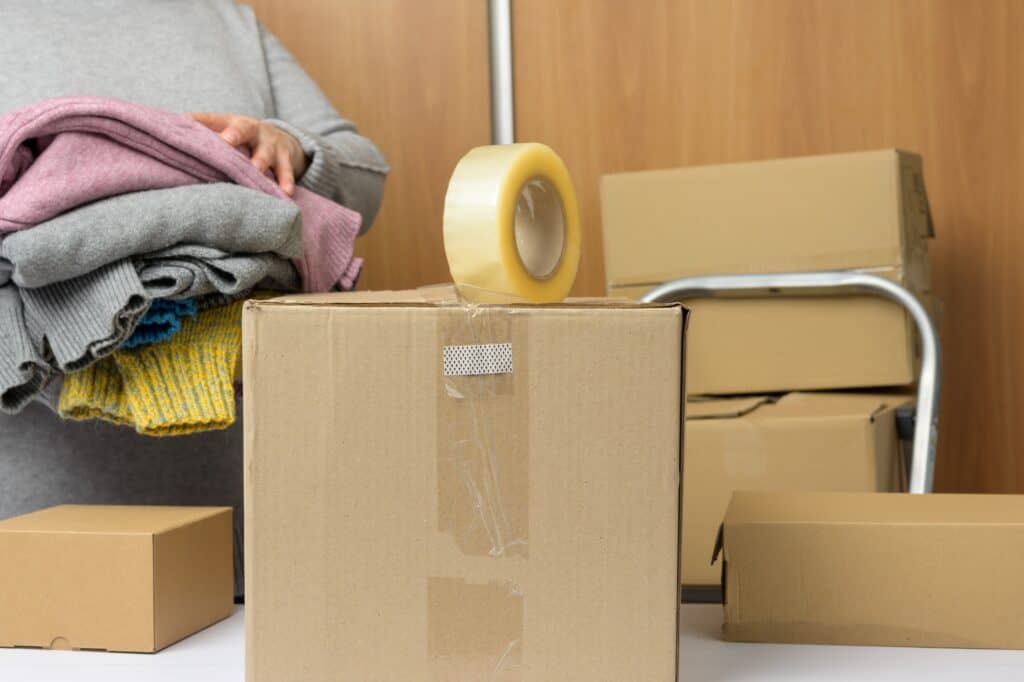 A woman in grey sweater packing clothes into cardboard boxes in the concept of 'differences between man and van and traditional removals'.