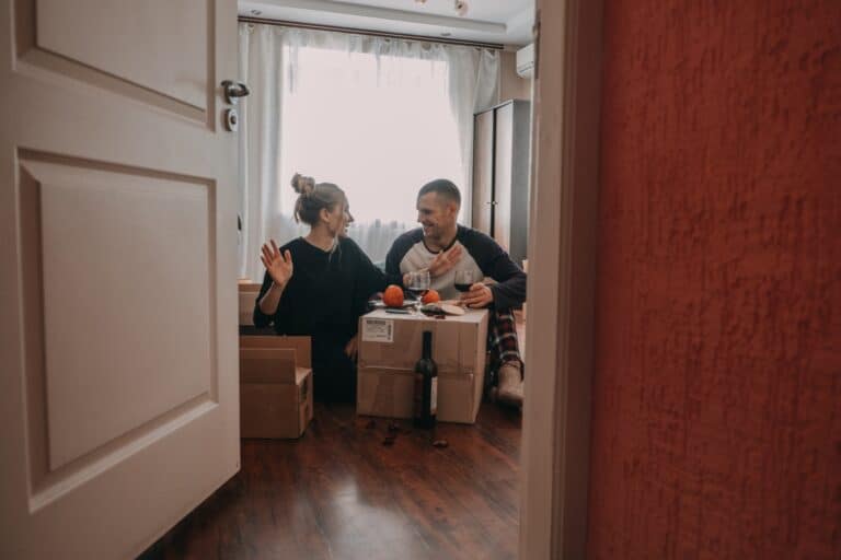 A couple surrounded by moving boxes in their new bedroom celebrating the move in the concept of 'How to Settle Into a New Home After Moving to Slough'.